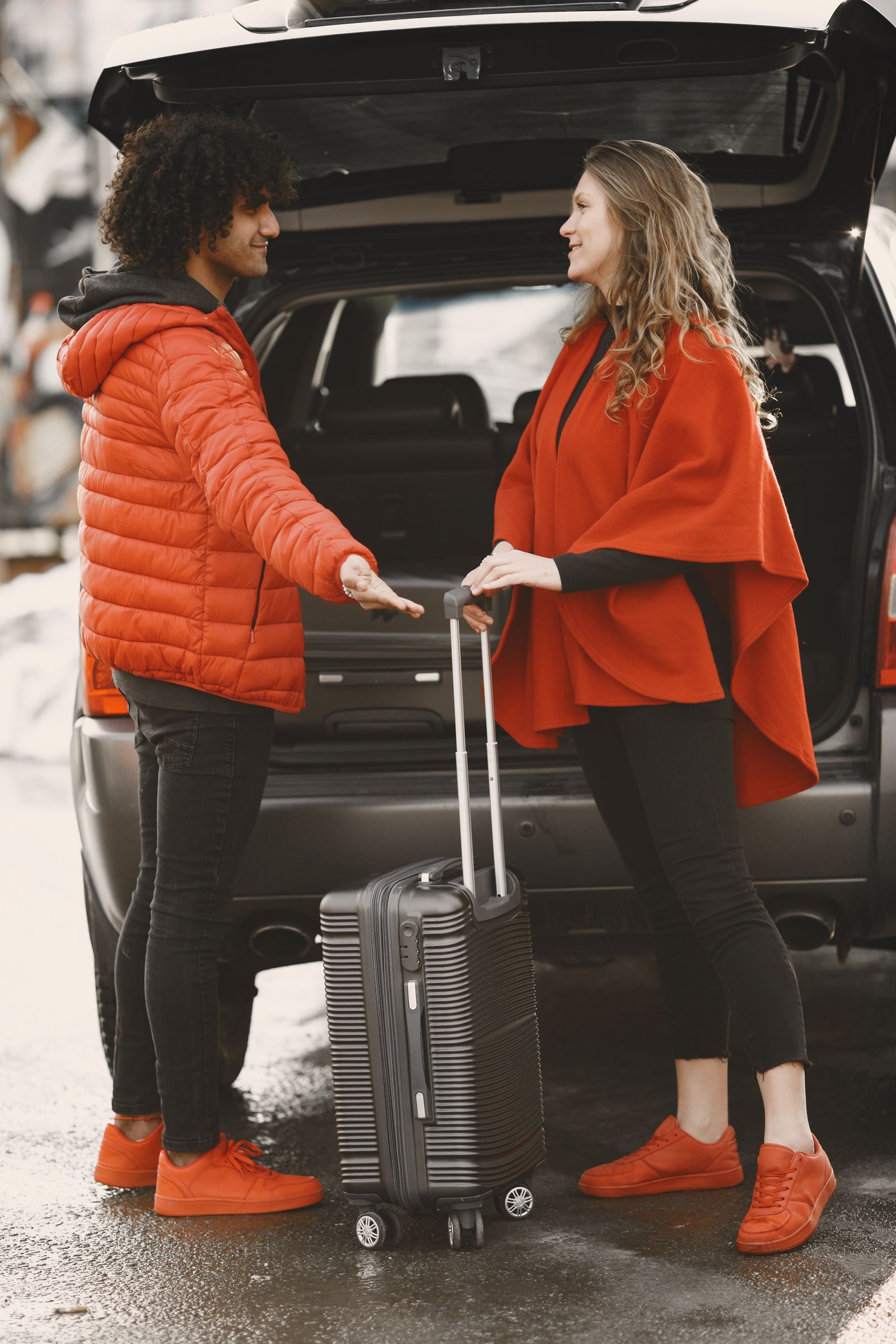 Two travellers standing at the back of a car, packing for a trip
